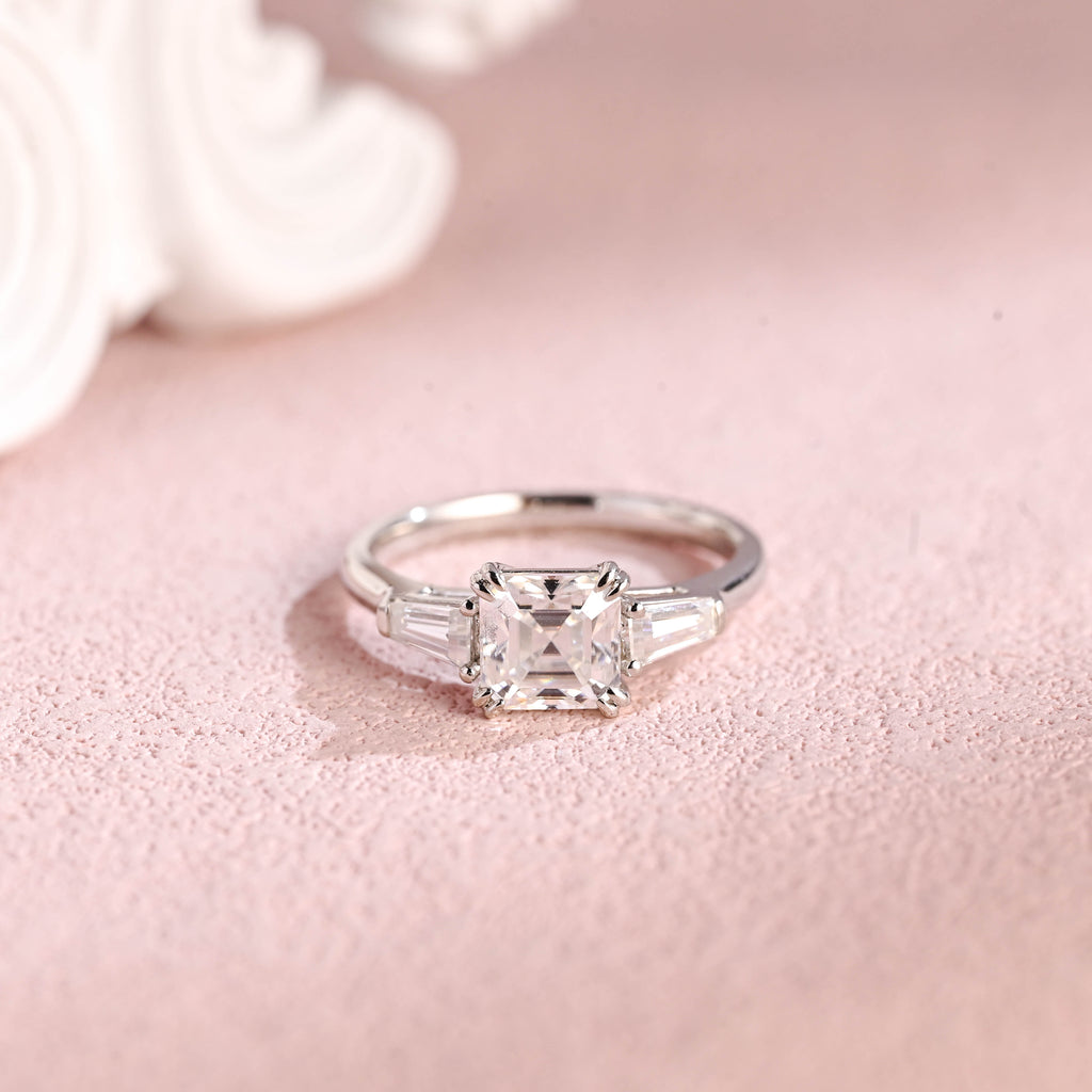 Front view of an IGI certified asscher cut lab grown diamond ring with side stones on a pink background.
