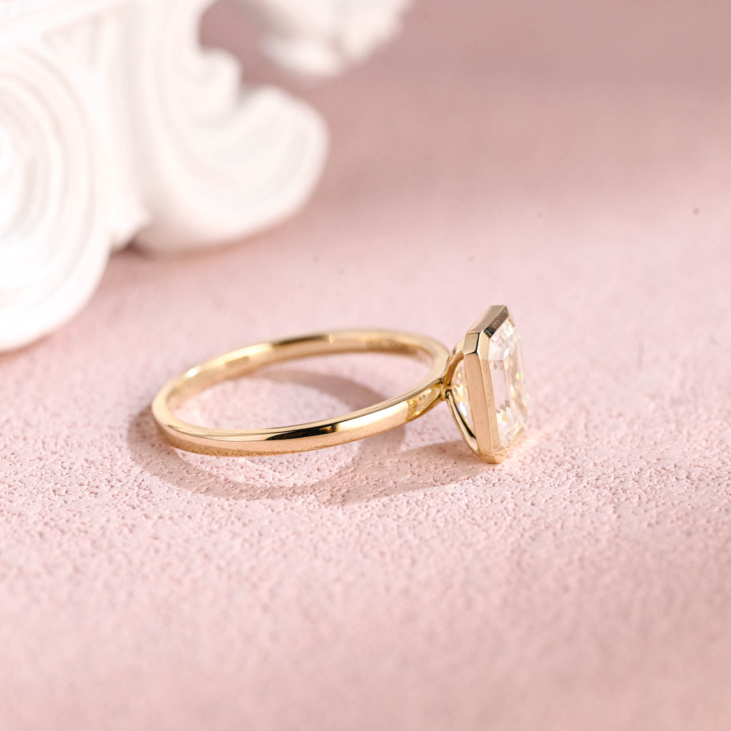 Side profile of a modern bezel set emerald cut lab diamond engagement ring.