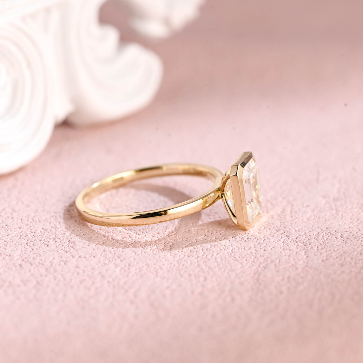 Side profile of a modern bezel set emerald cut lab diamond engagement ring.