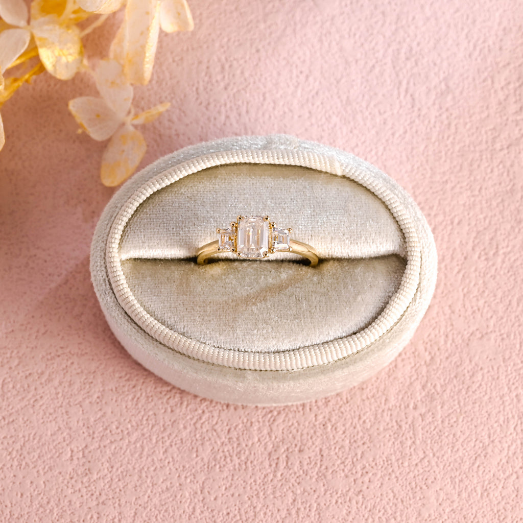 A classic 14k yellow gold three stone engagement ring featuring a large emerald cut lab grown diamond flanked by two step-cut side stones.