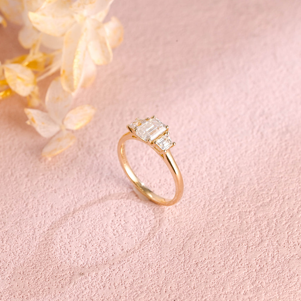 A classic 14k yellow gold three stone engagement ring featuring a large emerald cut lab grown diamond flanked by two step-cut side stones.