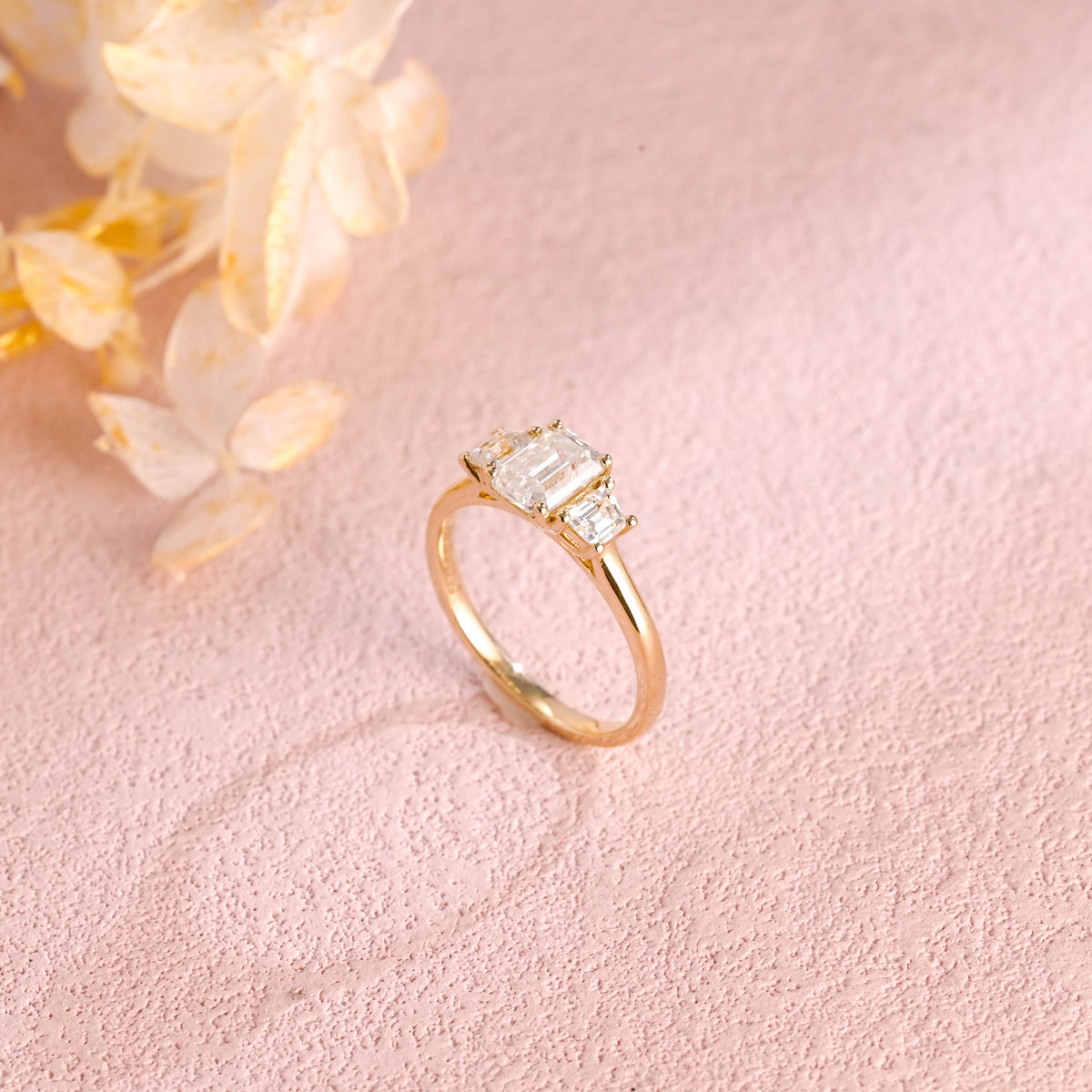 A classic 14k yellow gold three stone engagement ring featuring a large emerald cut lab grown diamond flanked by two step-cut side stones.