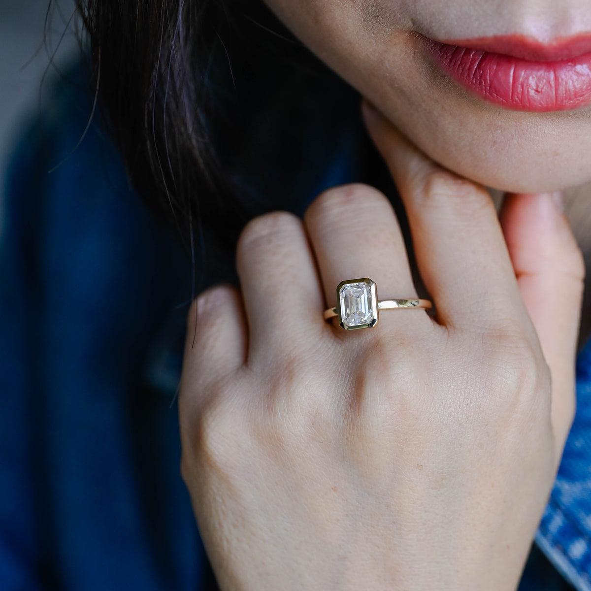 A model wearing a gorgeous bezel set emerald cut lab grown diamond ring on her finger.