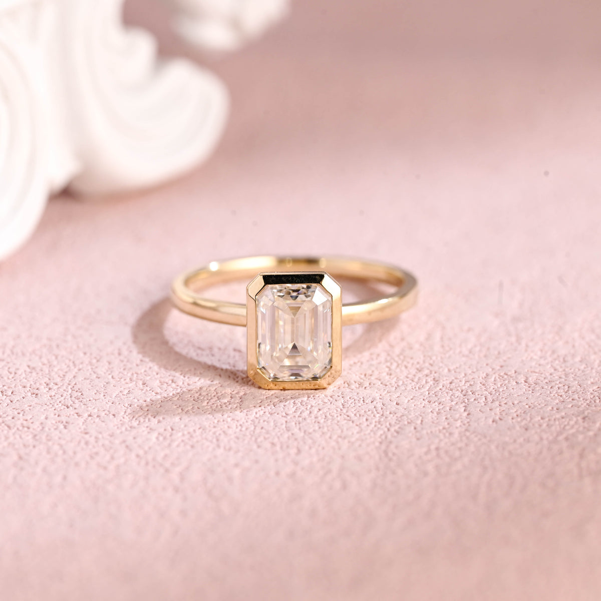 Front view of an IGI certified emerald cut lab grown diamond ring in a bezel setting on pink background.