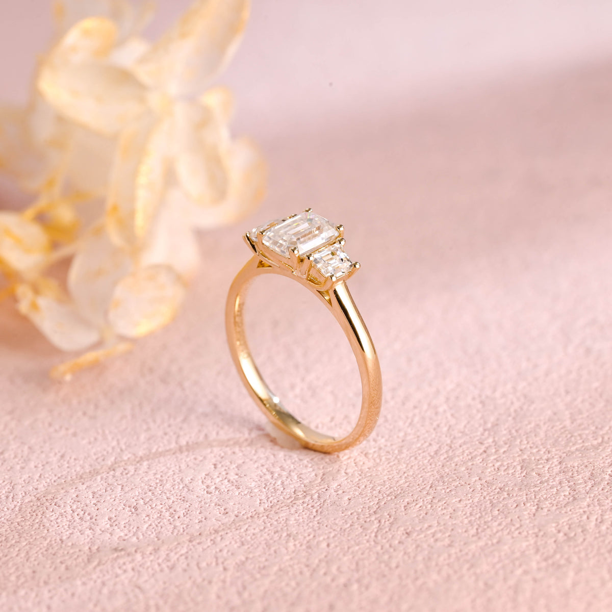 A classic 14k yellow gold three stone engagement ring featuring a large emerald cut lab grown diamond flanked by two step-cut side stones.